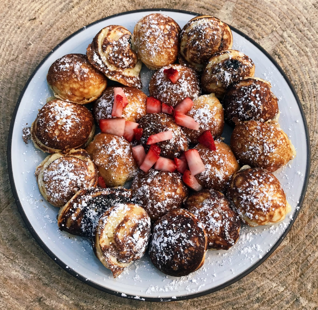 Picture of æbleskiver on a plate topped with cut up strawberries and powdered sugar.