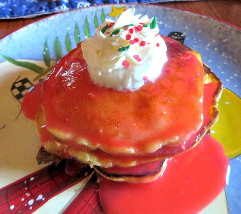 Picture of chunky apple pancakes topped with red hot syrup and whipped cream