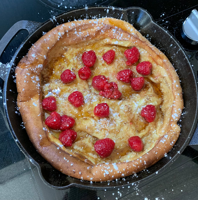 Picture of a german pancake in a cast iron pan. Topped with powdered sugar and raspberries.