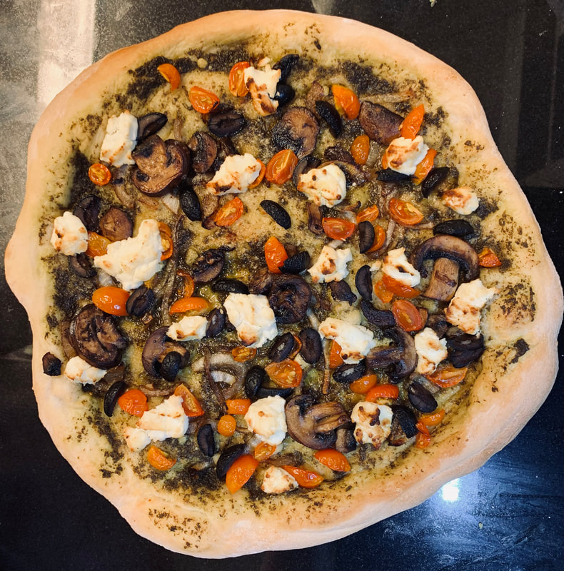 A goat cheese pesto pizza with diced cherry tomatoes, olives, mushrooms and sliced red onions.